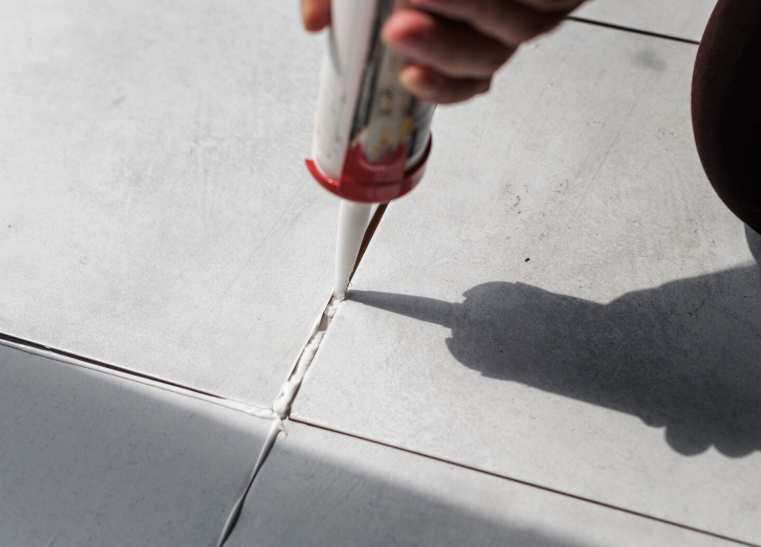 Applying sealant to tile seam during bathroom re-caulking and grout restoration