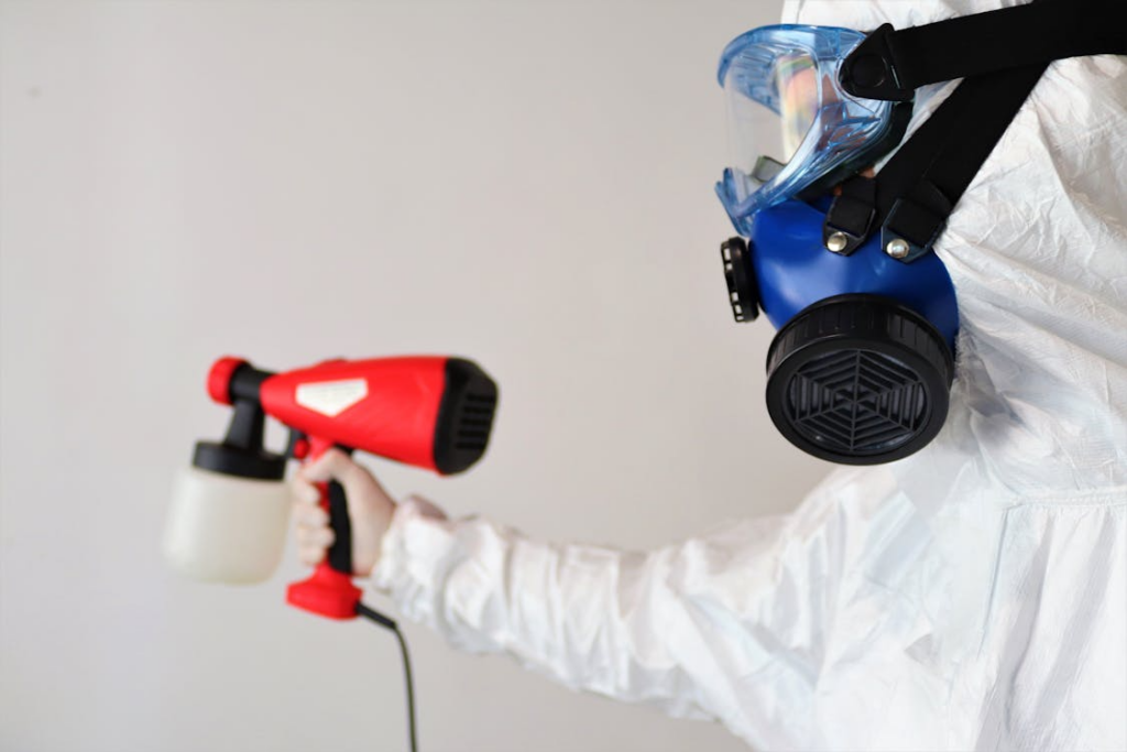 Mold remediation technician wearing protective gear spraying antimicrobial treatment indoors