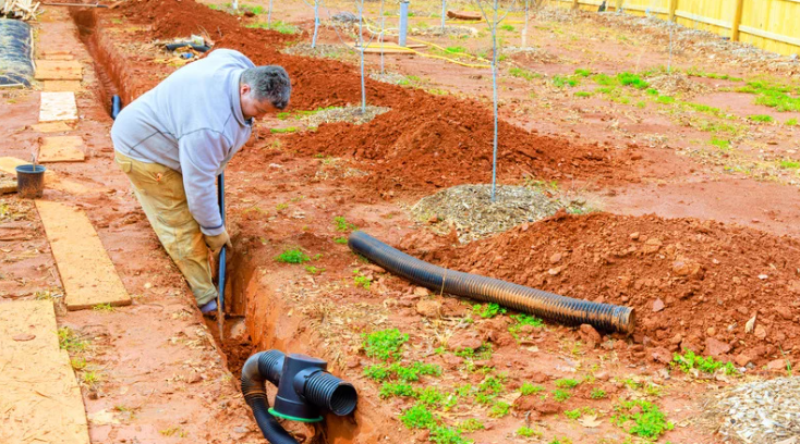 Contractor installing French drain pipe as part of backyard drainage solutions system